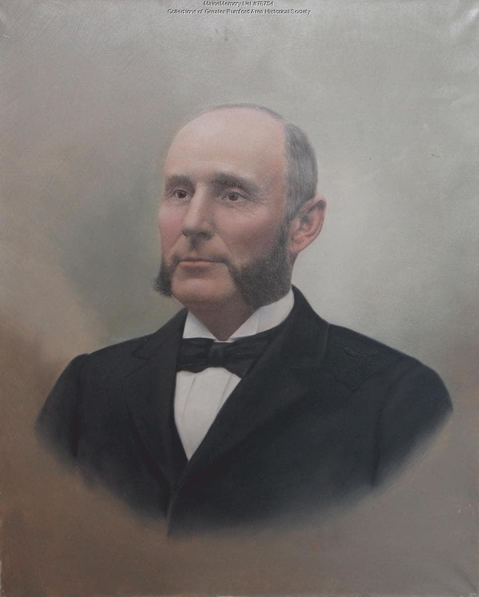 Studio portrait of a bearded man in a dark suit and tie, seated and facing the camera.