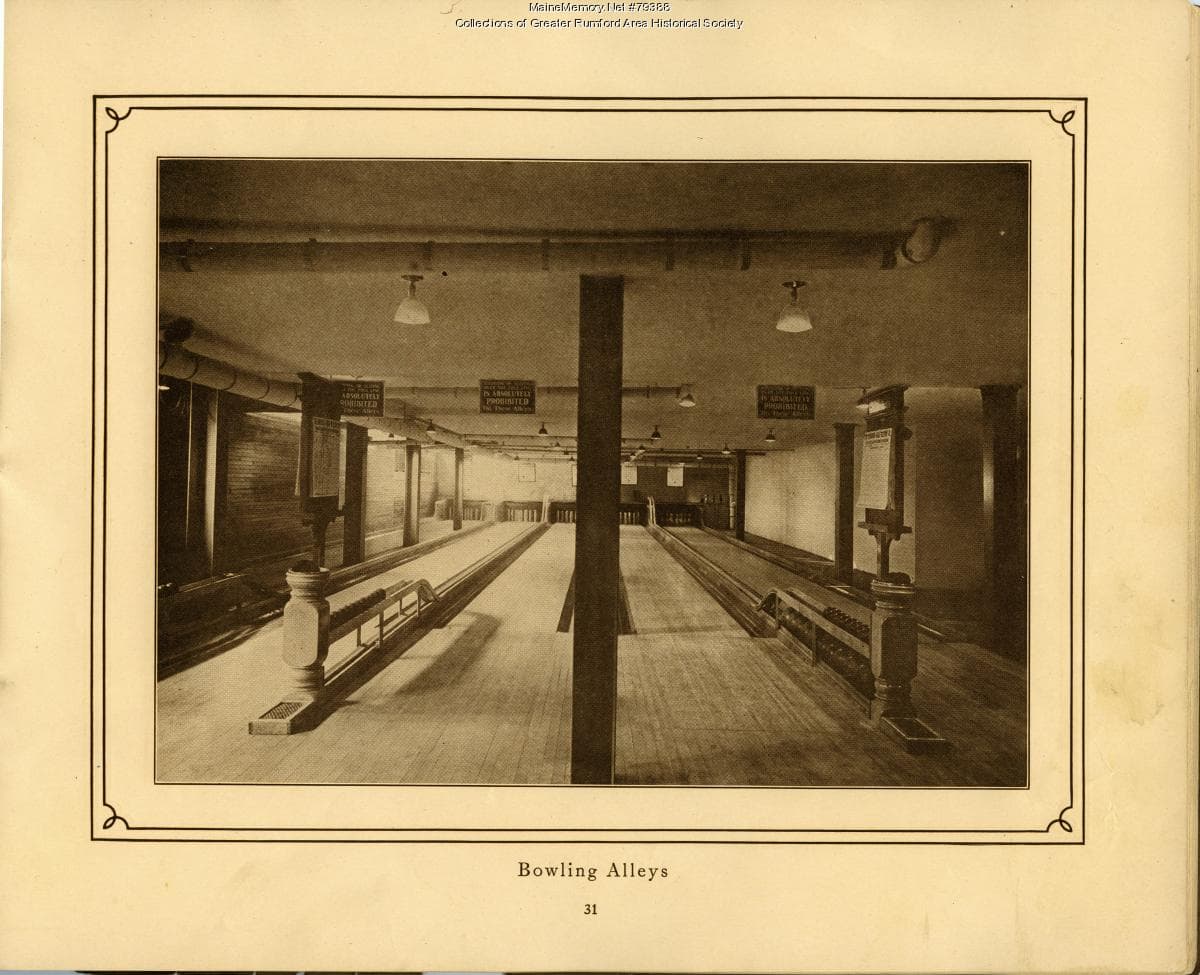 Interior of a basement bowling alley with wooden lanes receding toward pins at the far end.